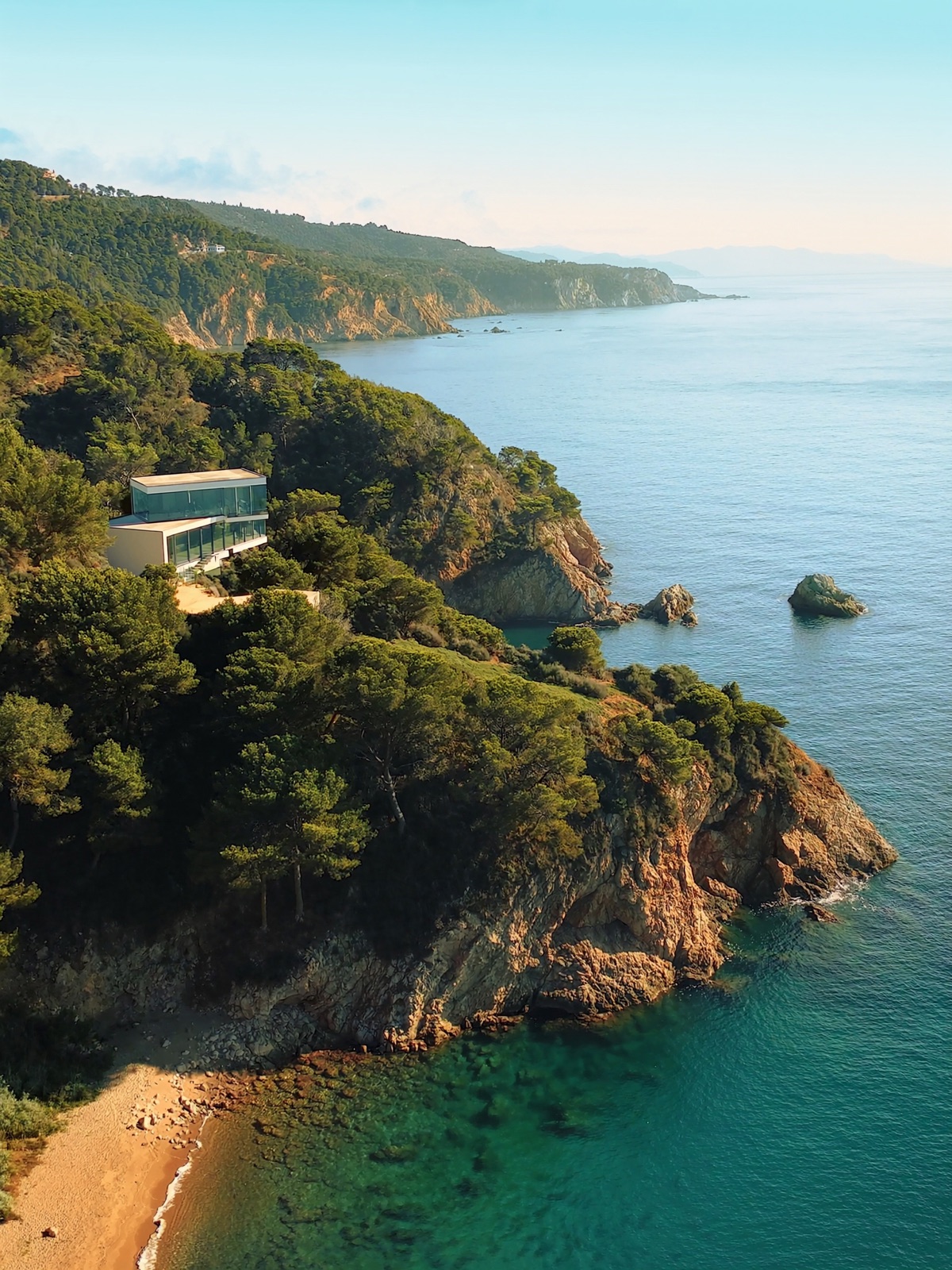 A pine-covered rocky Costa Brava coastline above a secluded emerald cove
