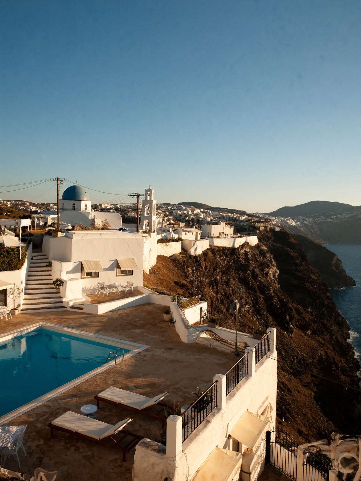 A whitewashed Cycladic village with blue domes above the Aegean at sunset