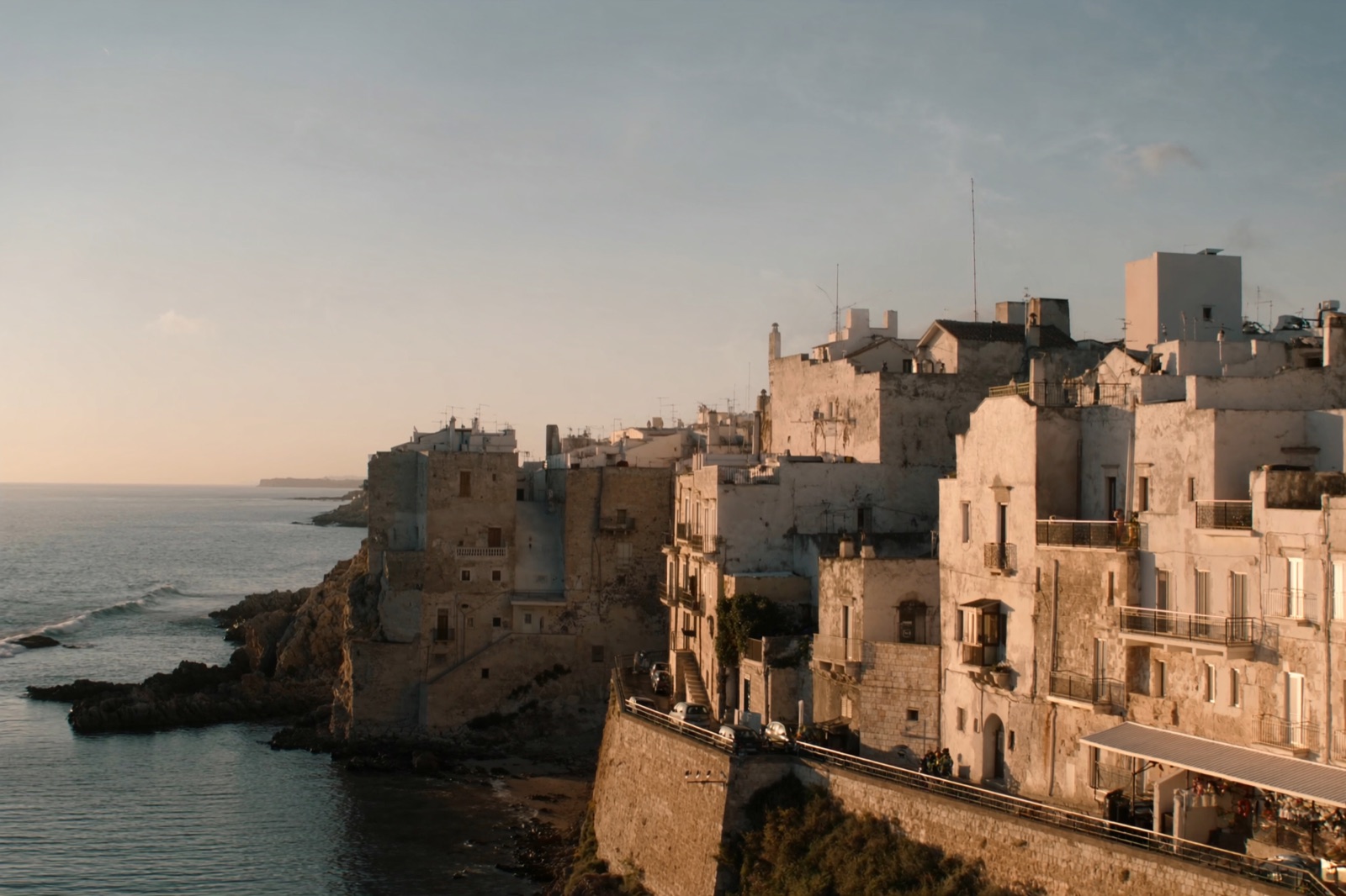 A whitewashed Puglian coastal town above the calm turquoise Adriatic at golden hour