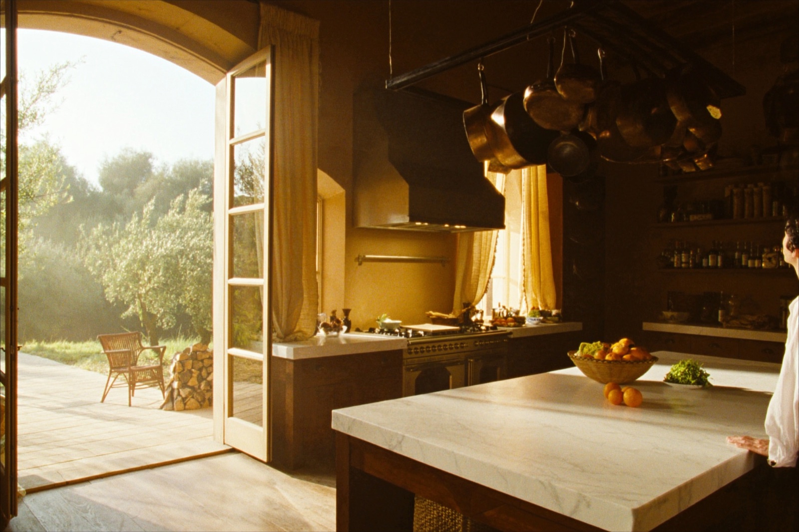 A rustic-luxury Mediterranean villa kitchen with a large range, marble island and copper pots open to a terrace